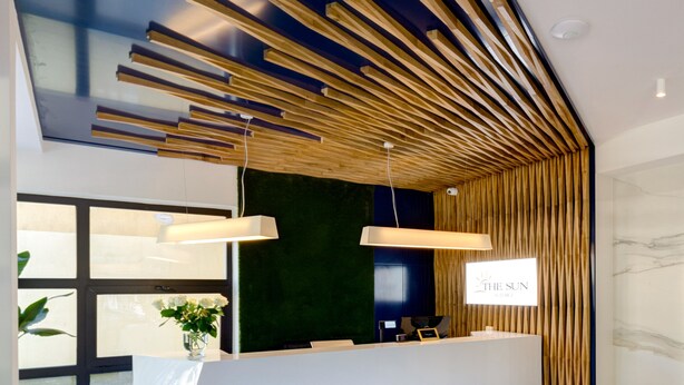 A modern reception desk with a sleek white design, a dark green wall, and a wooden slatted ceiling.