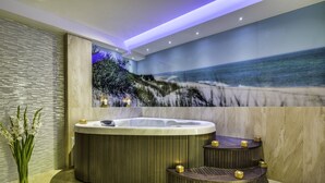 A modern bathroom with a large bathtub, a small seating area, and a mural of a beach scene.