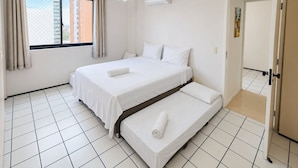 Una camera d'albergo con un letto, una finestra con tende, un condizionatore d'aria e un pavimento piastrellato.