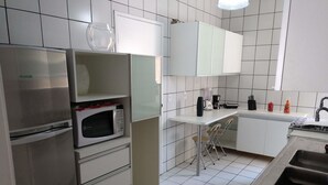 Una cocina moderna con un refrigerador de acero inoxidable, un microondas y un lavamanos. Hay armarios blancos y un taburete pequeño.