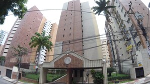 Un edificio de varios pisos con entrada protegida por una reja, un reloj y un letrero que indica zona prohibida para estacionar.