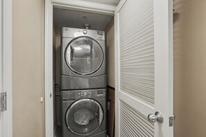 Une buanderie équipée de deux machines à laver à chargement frontal superposées et d’une porte à persiennes.