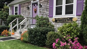 En hytte med træfacade, lilla skodder og et skilt, der siger "Mermaid Cottage".
