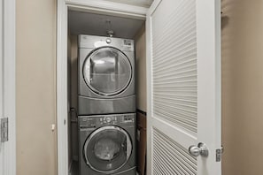 Un lavadero con dos lavadoras de carga frontal apiladas y una puerta con diseño persiana.