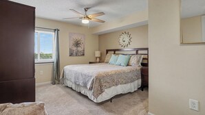 A bedroom with a bed, a ceiling fan, a window with curtains, and a wall-mounted mirror.