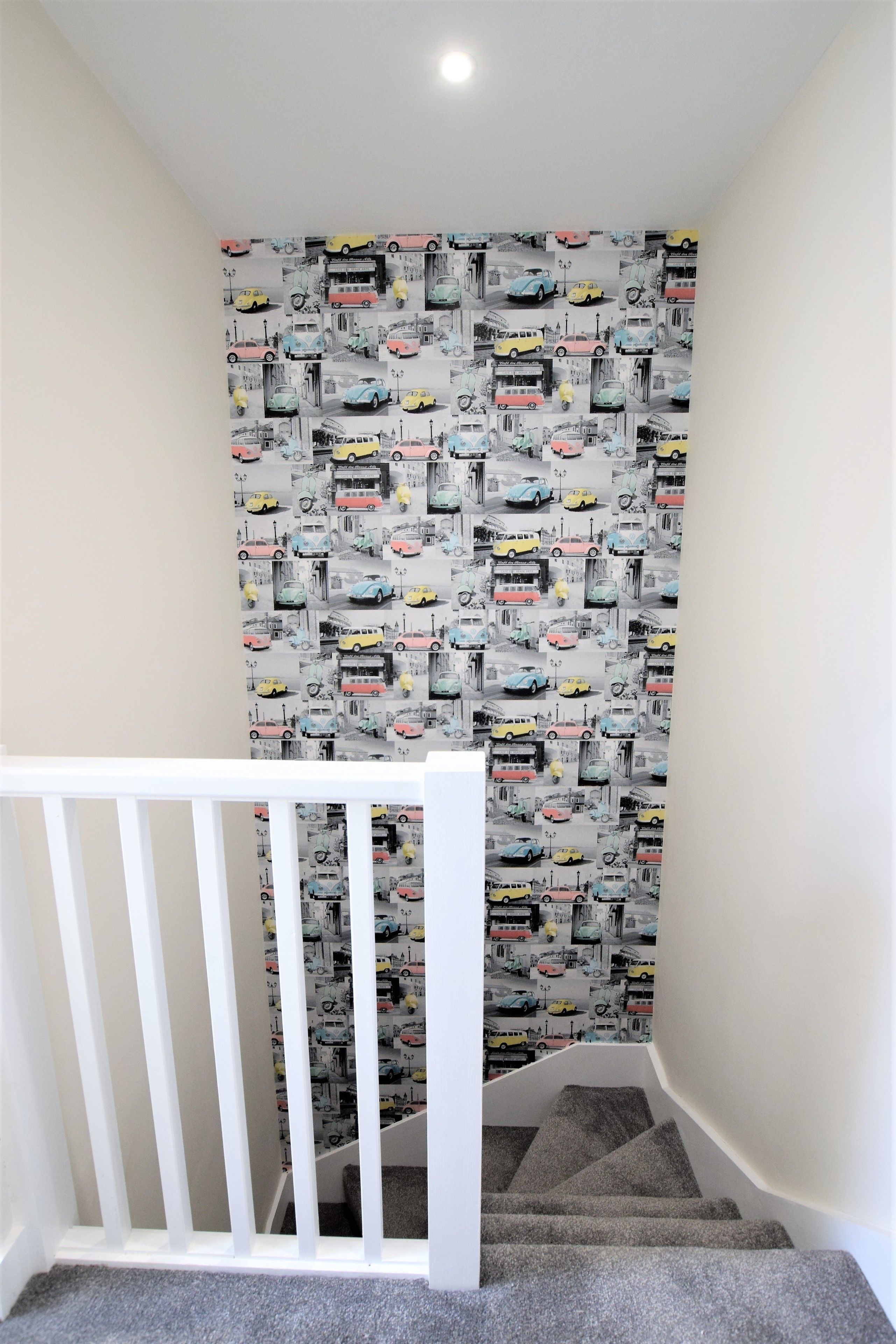 A staircase with a white railing and carpeted steps leading to a room with a wall covered in a pattern of vintage cars.