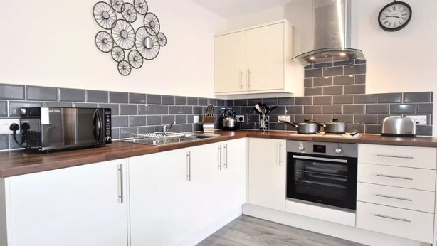 A modern kitchen with white cabinets, a stainless steel range hood, a microwave, and a built-in oven. - The Old Bank - yourapartment (Bristol)