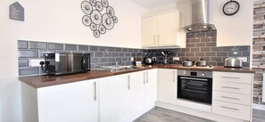 A modern kitchen with white cabinets, a stainless steel range hood, a microwave, and a built-in oven. - The Old Bank - yourapartment (Bristol)
