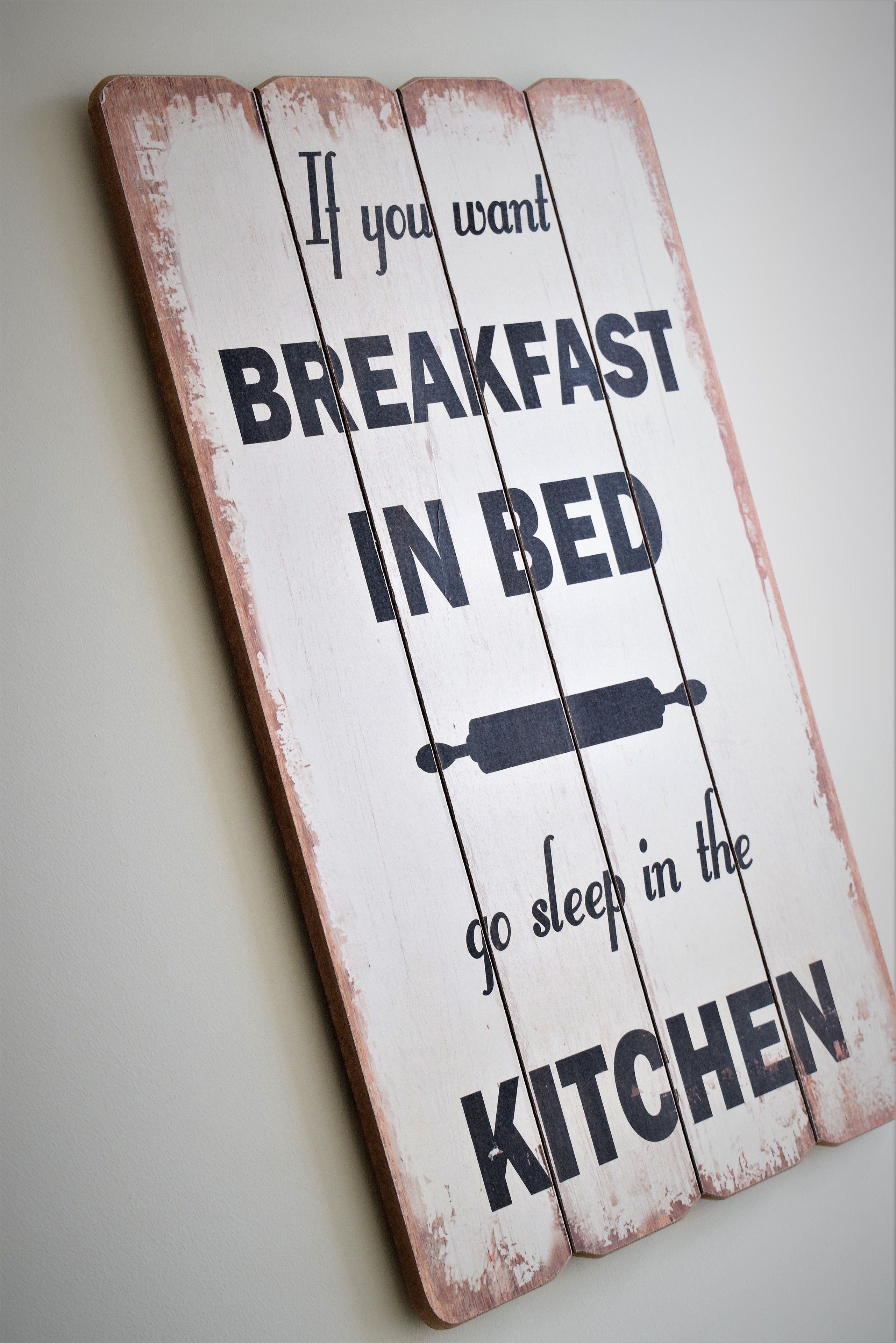 A rustic wooden sign with the text "If you want breakfast in bed, go sleep in the kitchen."