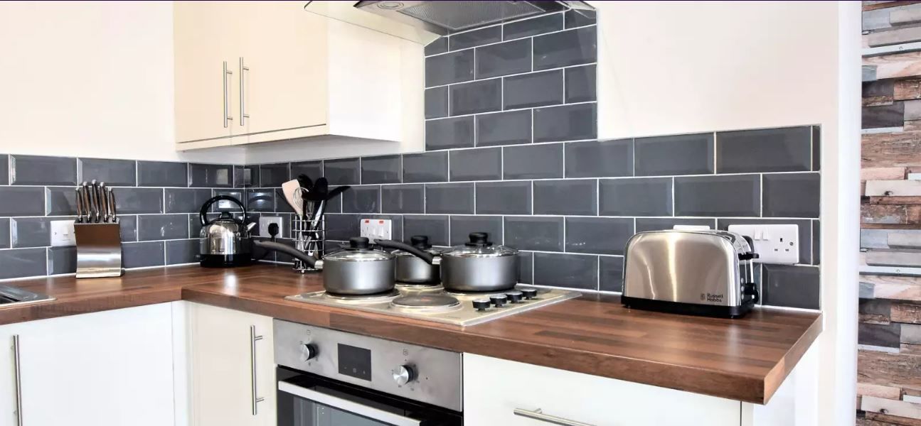 A modern kitchen with a wooden countertop, stainless steel appliances, and black and white tiled backsplash.