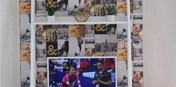 Una habitación con un televisor sobre un mueble bajo, un estante con objetos diversos y un papel tapiz decorado.