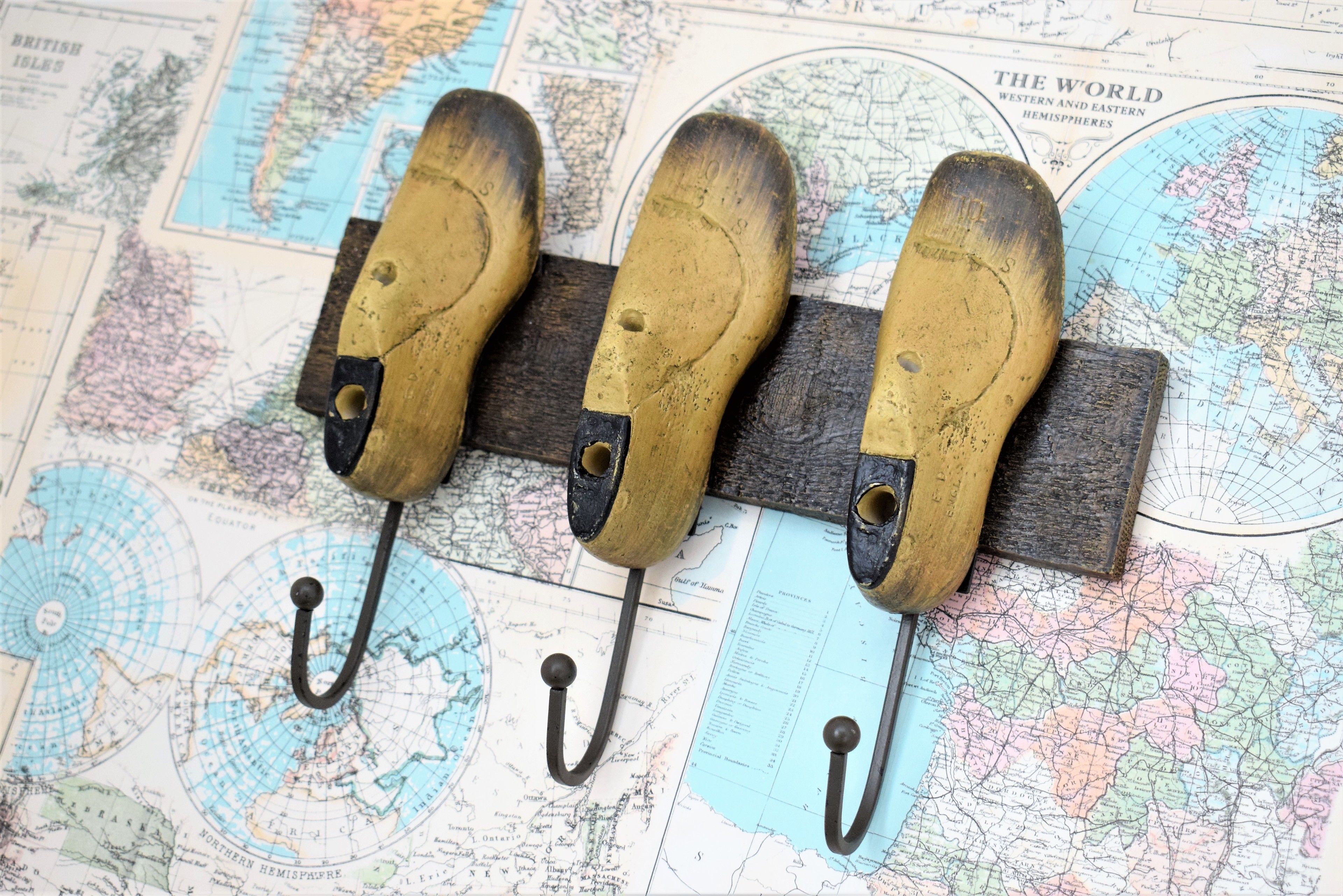 A wooden pegboard with three metal hooks against a background of old maps.