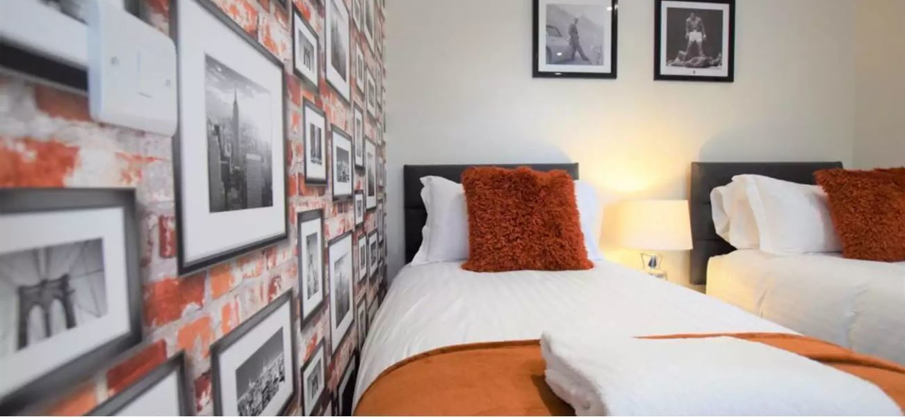 A hotel room with two beds, a brick-patterned wall, and framed pictures.