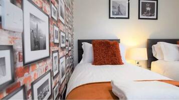 A hotel room with two beds, a brick-patterned wall, and framed pictures.