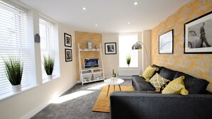 A modern living room with a grey sofa, a coffee table, and a bookshelf. - The Old Bank - yourapartment (Bristol)