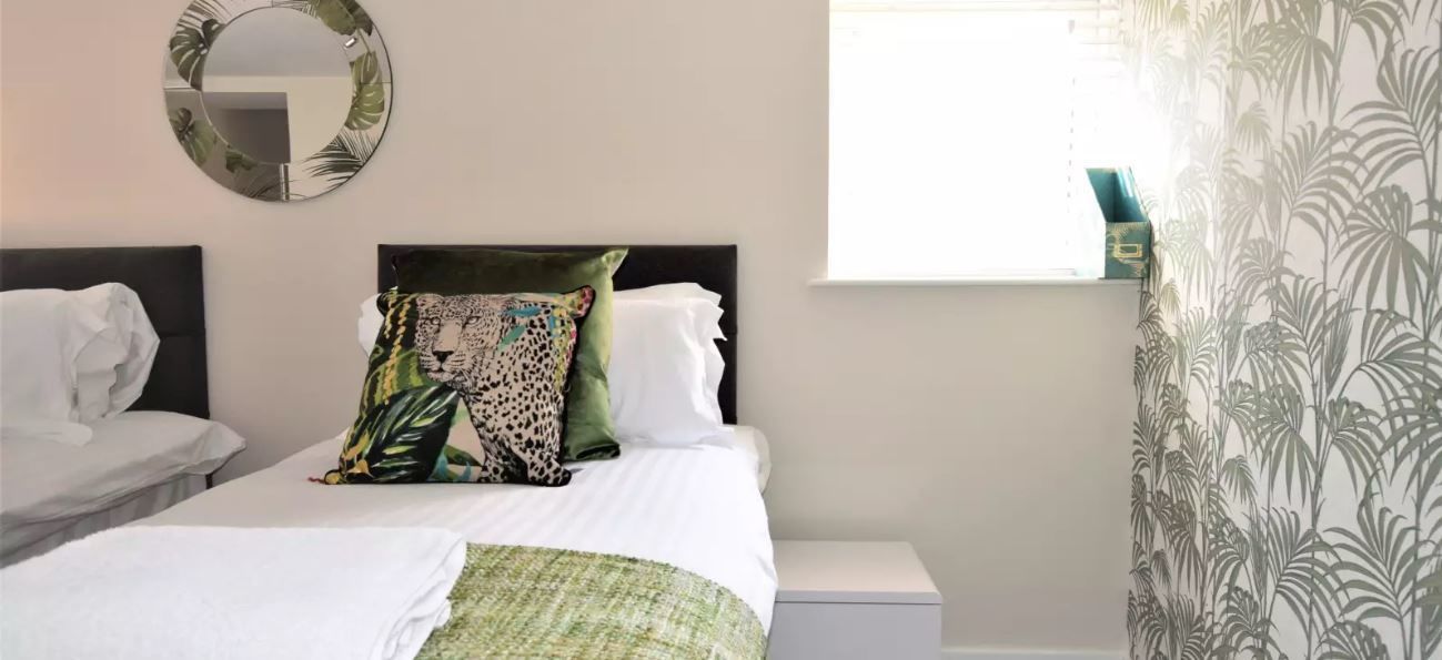 Una habitación de hotel con una cama, una mesita de noche, un espejo y una ventana con cortinas.