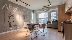 A modern kitchen with a dining area, featuring a large window, wooden cabinets, and a concrete wall with a drawing. - Ares Aparthotel (Cluj-Napoca)