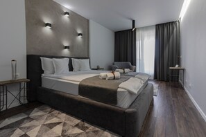 A modern hotel room with a large bed, a bedside table, a chair, and a small table with a lamp. - Ares Aparthotel (Cluj-Napoca)