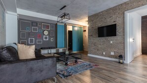 A modern living room with a grey sofa, a coffee table, and a colorful rug. There is a blue door and a brick wall with a mounted TV. - Ares Aparthotel (Cluj-Napoca)