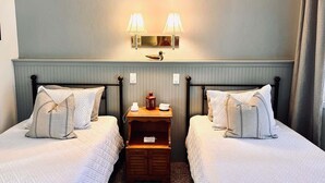A hotel room with two beds, a nightstand, and a wall-mounted lamp.