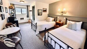 A hotel room with two beds, a dining table, and a small kitchen area.