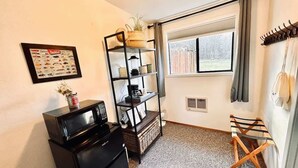 A compact living space with a kitchenette, a bookshelf, a small table, and a window with curtains.