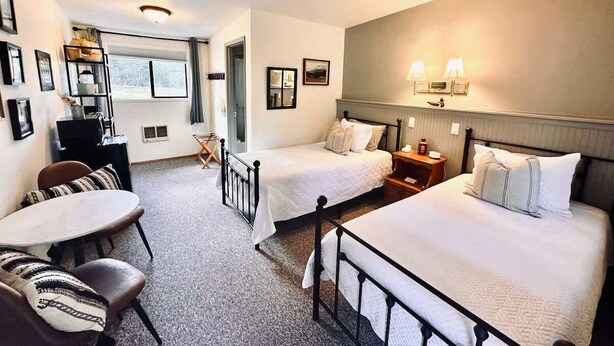 A hotel room with two beds, a dining table, and a small seating area.