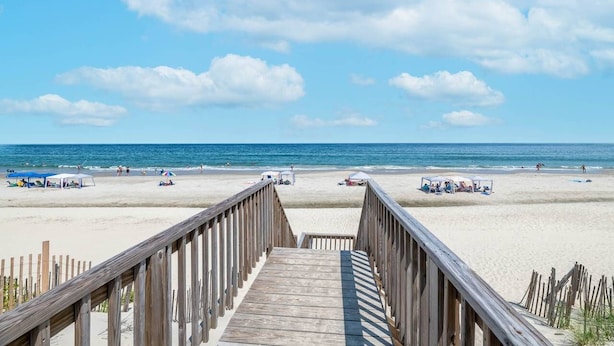 Una passerella di legno che conduce a una spiaggia sabbiosa con ombrelloni e bagnanti.