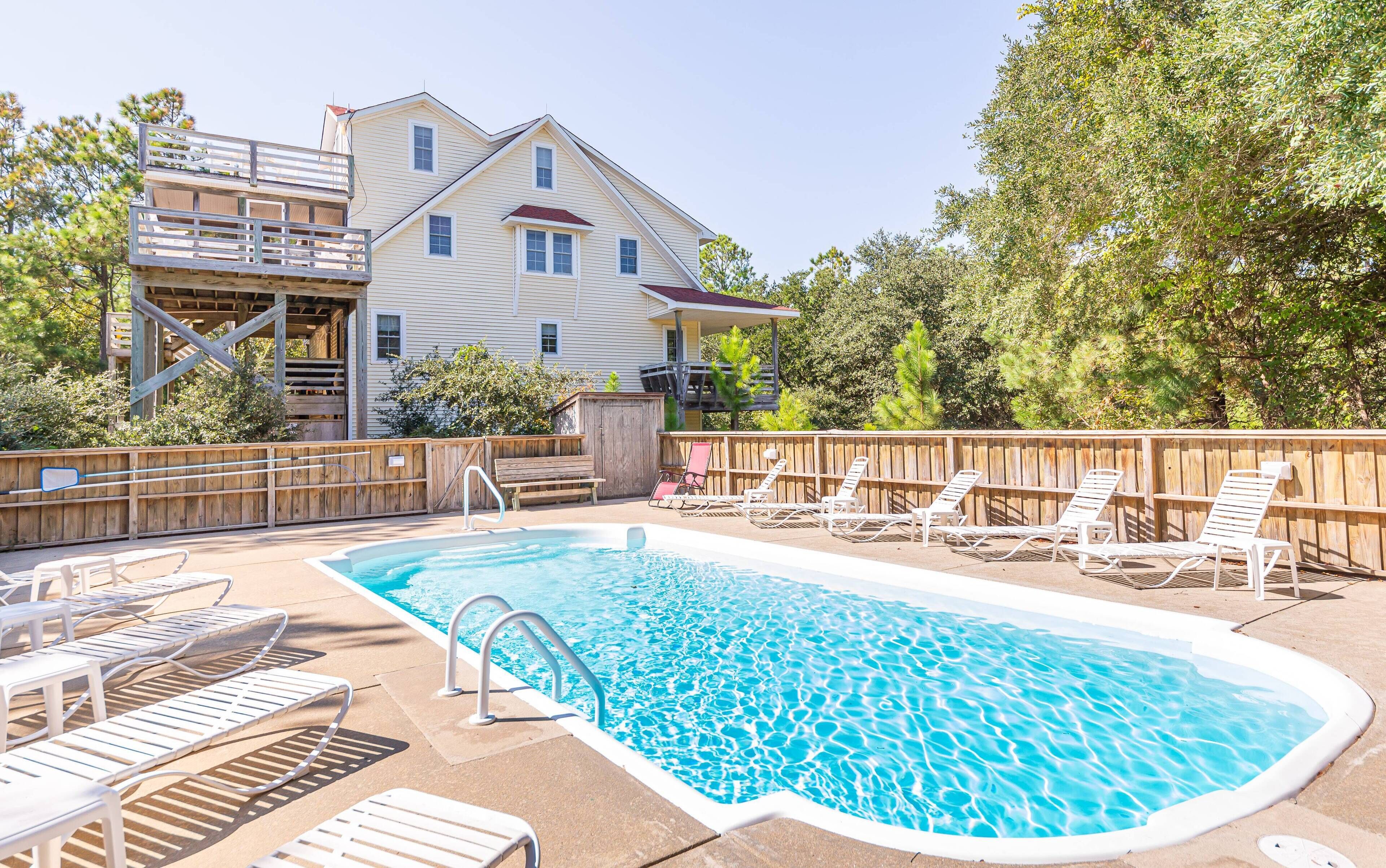 Ein Schwimmbad mit Liegestühlen, einer Holzterrasse und einem Haus im Hintergrund.