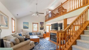 Un ampio soggiorno con camino, una scala in legno e un grande televisore.