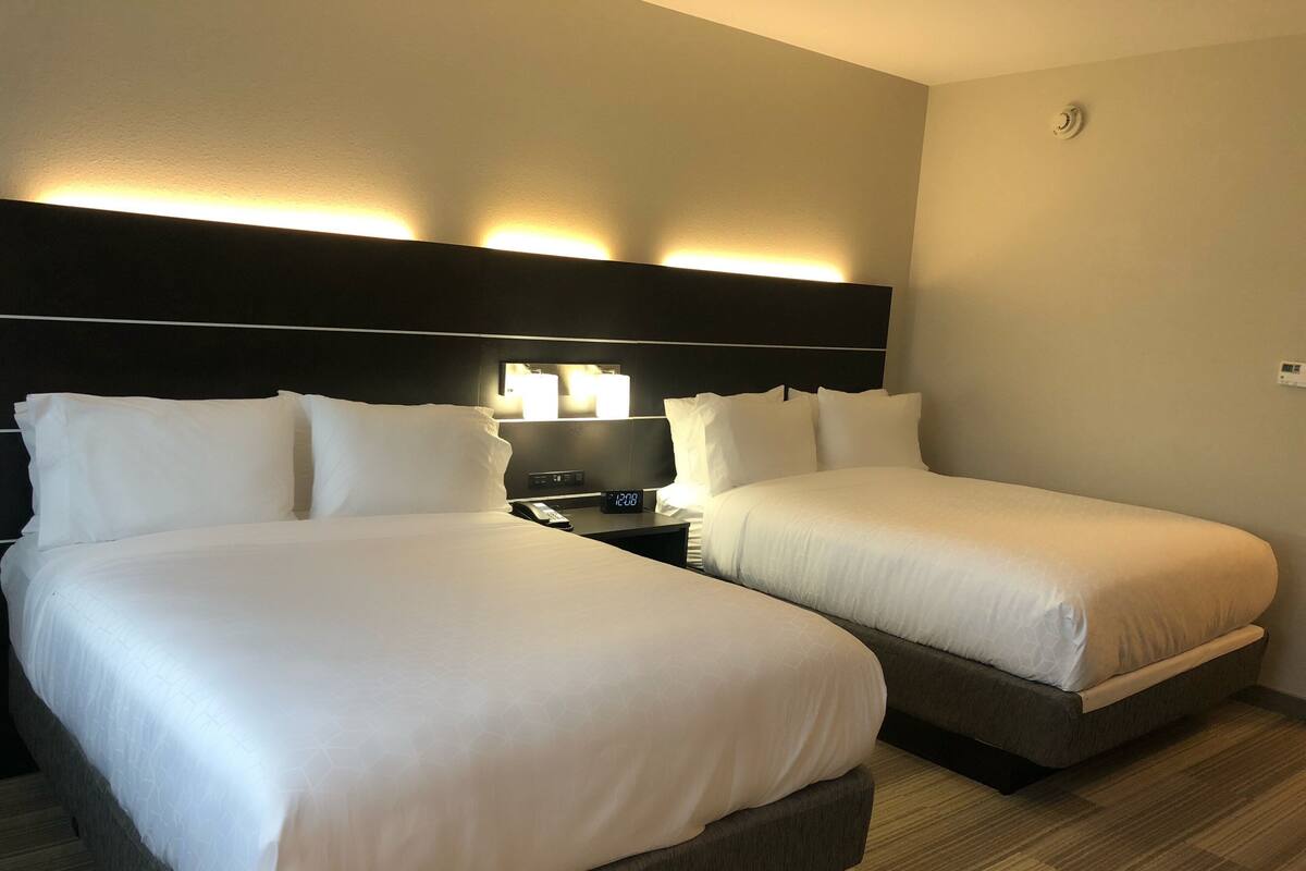 A hotel room with two beds, a nightstand with a lamp, and a wall-mounted light fixture.