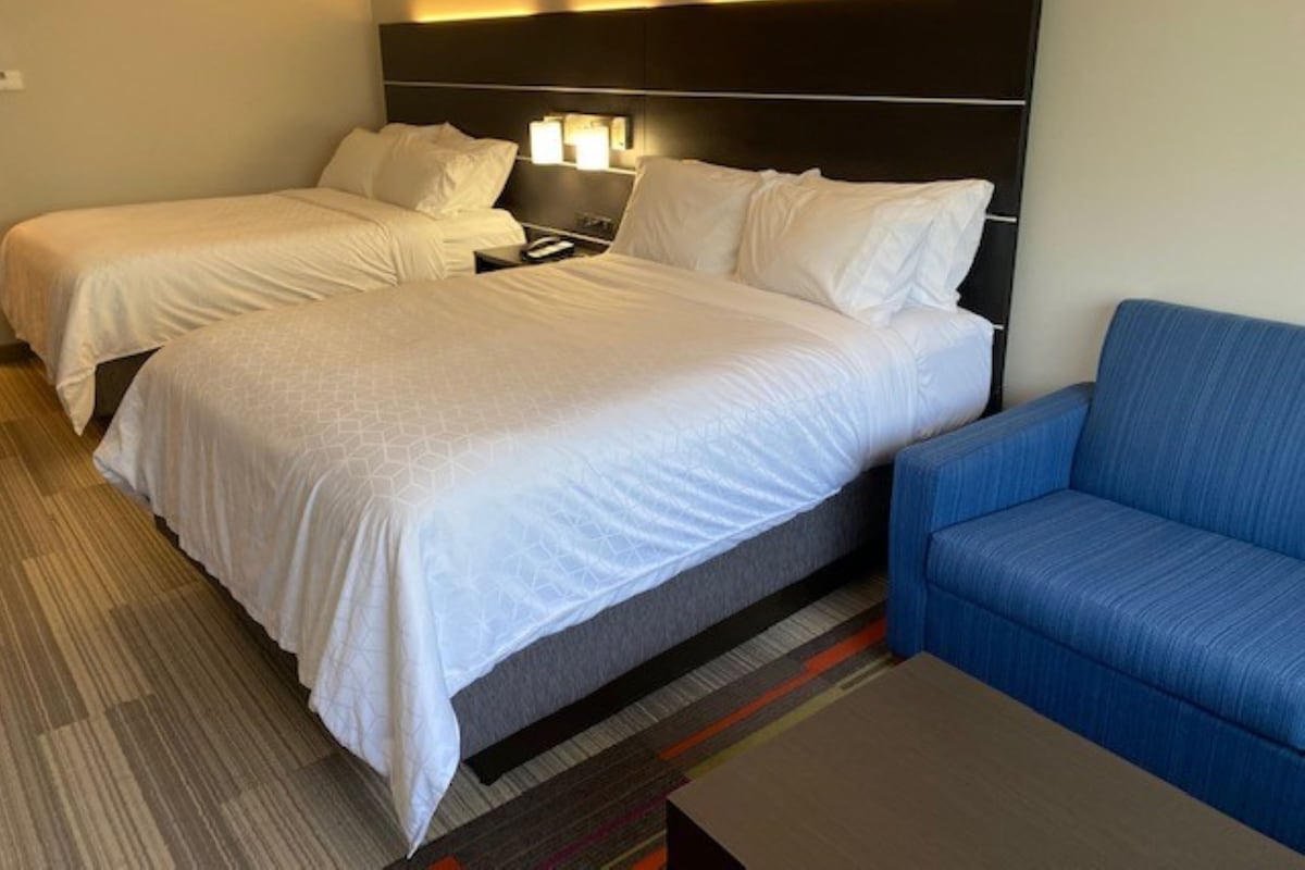 A hotel room with two beds, a sofa, and a nightstand with a lamp.