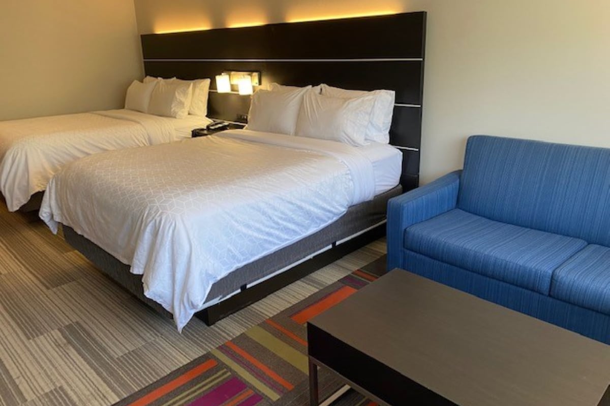 A hotel room with two beds, a blue sofa, and a small table.