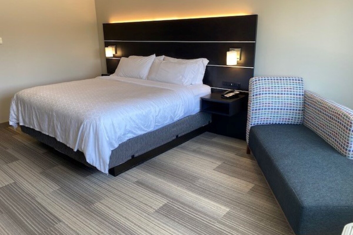 A hotel room with a bed, bedside table, and a chair.