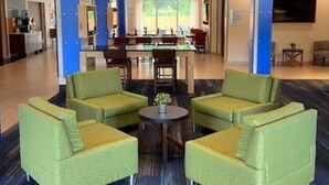 Eine Lobby mit grünen Sesseln, einem Couchtisch und einer Bar im Hintergrund.