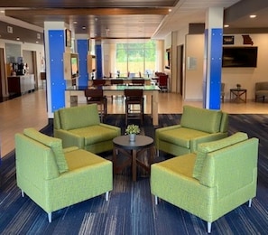 A lobby with green armchairs, a coffee table, and a bar area in the background.