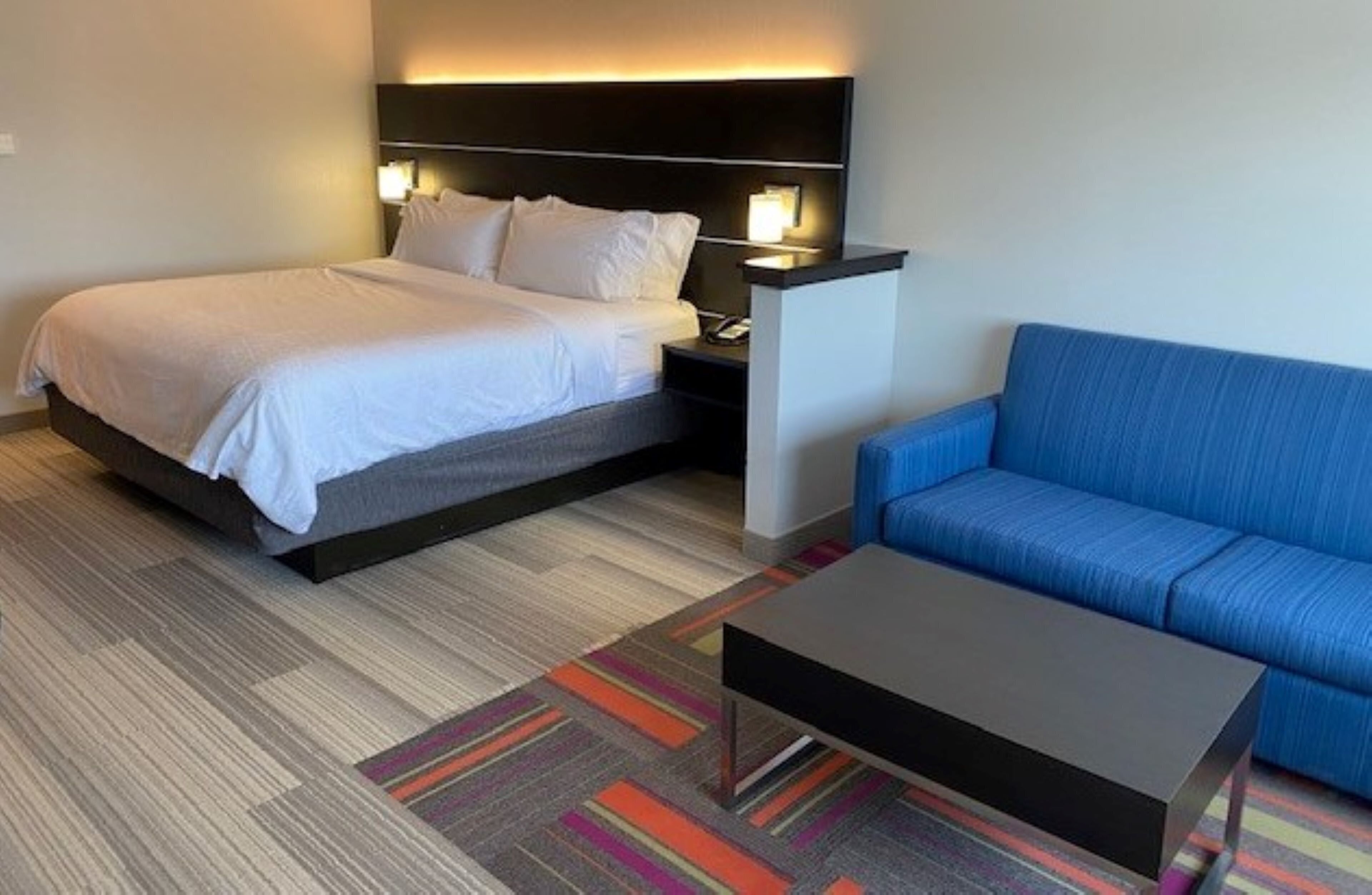 Una habitación de hotel con una cama, un sofá azul, una mesita y una lámpara en la mesita de noche.