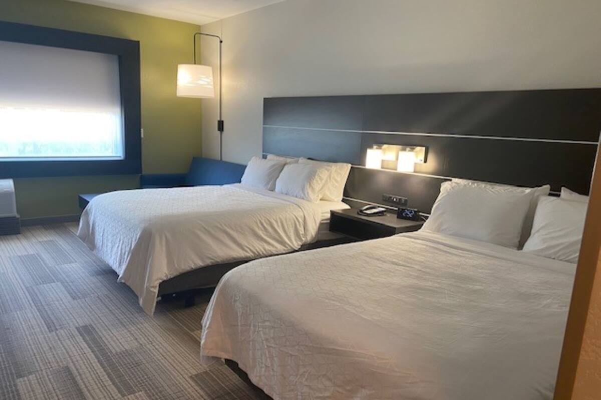 A hotel room with two beds, a nightstand, a lamp, and a window with blinds.