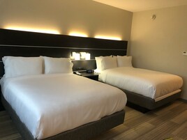 A hotel room with two beds, a nightstand with a lamp, and a wall-mounted light fixture.