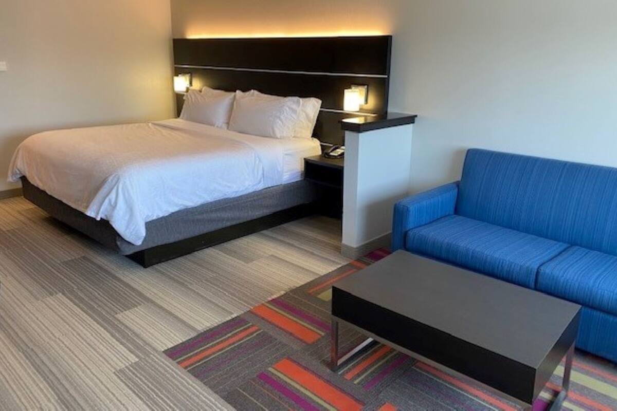 A hotel room with a bed, a blue sofa, a small table, and a colorful striped rug.