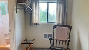 Ein Eckzimmer mit einem Holzstuhl, einem Wäscheständer aus Metall und einem fenster mit Vorhängen.