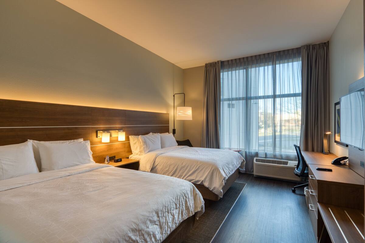 A hotel room with two beds, a desk, a chair, a TV, and a window with curtains.