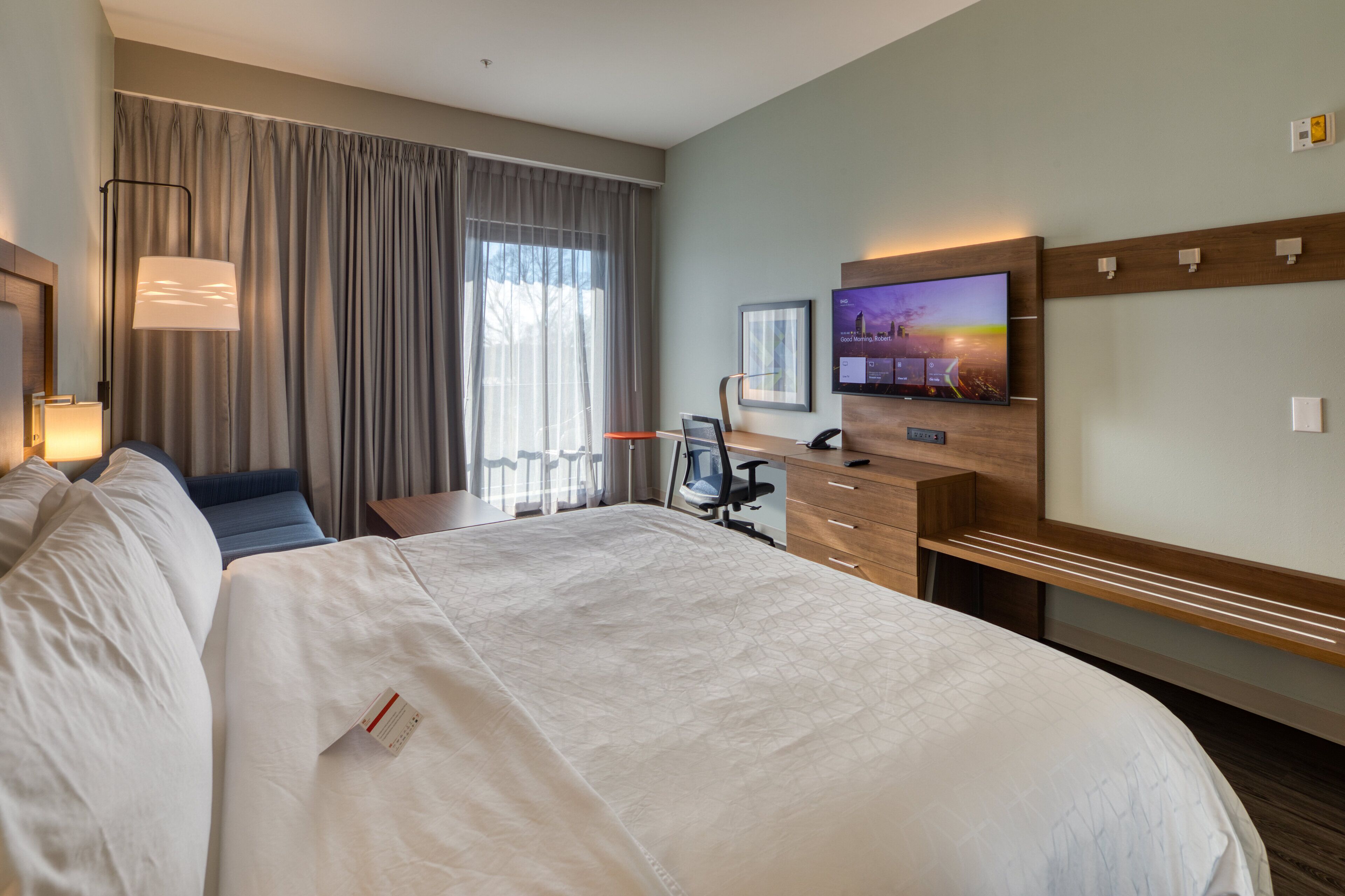 Een hotelkamer met een groot bed, een bureau met stoel, een televisie en een raam met gordijnen.