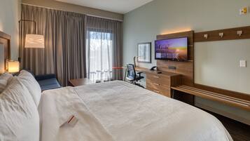 Een hotelkamer met een groot bed, een bureau met stoel, een televisie en een raam met gordijnen.