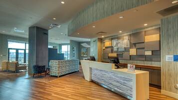 Un espace d’accueil d’hôtel au design moderne, comprenant un comptoir d’accueil, un coin salon et de grandes fenêtres laissant entrer la lumière naturelle.