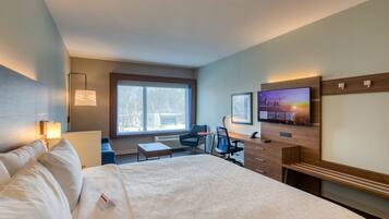 A hotel room with a large bed, a desk, a chair, a TV, and a window.