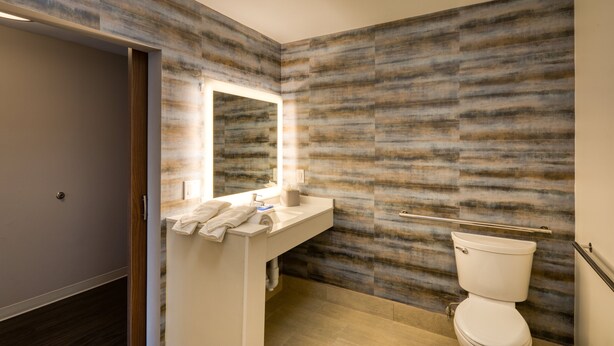 Un baño moderno con piso de madera, un lavamanos blanco con espejo y un inodoro.