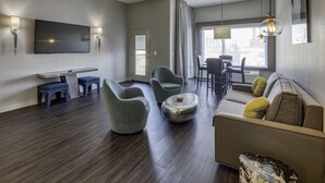 Una sala de estar moderna con una televisión de pantalla plana, dos sillones, un sofá, una mesa de comedor con sillas y un amplio ventanal con cortinas.