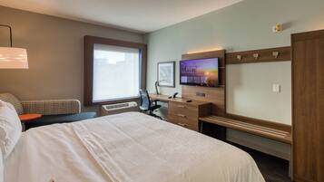 A hotel room with a large bed, a desk, a chair, a television, and a window.