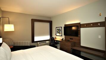 A hotel room with a bed, a desk, a chair, a television, and a window with blinds.